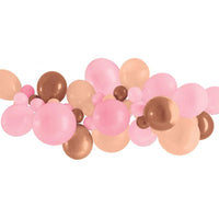 Assembled rose gold balloon garland curving across a party dessert table